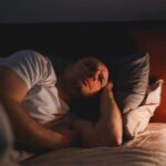 Exhausted person lying awake in bed despite feeling extremely tired