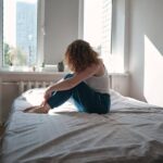 Person sitting on the edge of a bed feeling disconnected after waking up