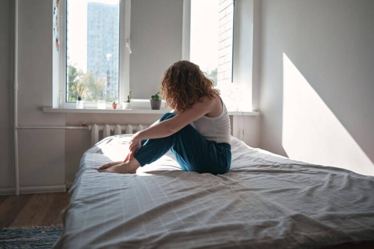 Person sitting on the edge of a bed feeling disconnected after waking up