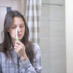 Person touching forehead while brushing teeth in the bathroom