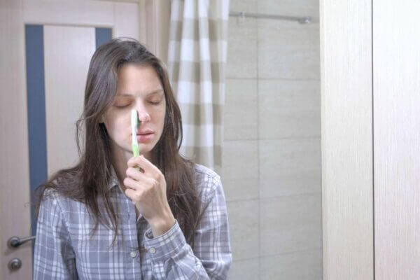 Person touching forehead while brushing teeth in the bathroom