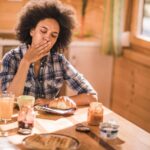 Person feeling nauseous shortly after eating breakfast at a kitchen table