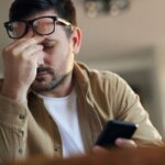 Person getting a headache after scrolling on a smartphone in a dark room