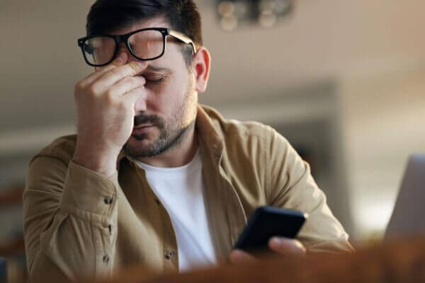 Person getting a headache after scrolling on a smartphone in a dark room