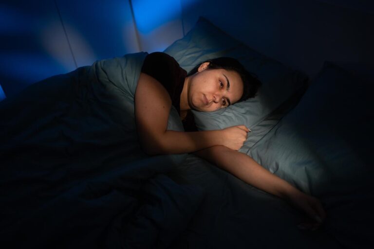 “Tired person lying in bed awake at night despite feeling exhausted”