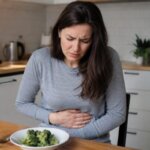 Western woman holding her stomach with abdominal pain after eating broccoli