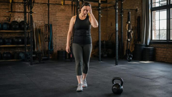 Person recovering after kettlebell swings and feeling lightheaded in a gym