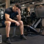 Man sitting on a leg press machine with a hand on his temple after a heavy set
