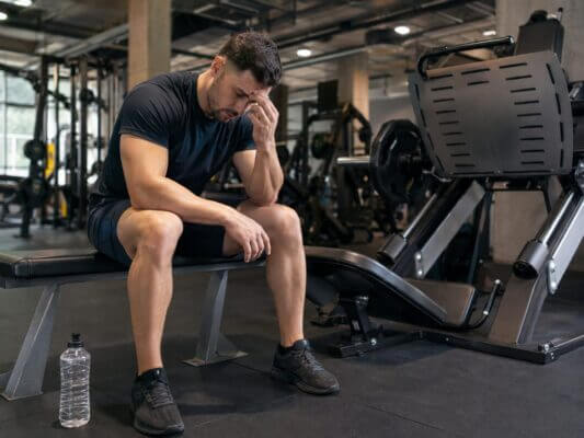 Man sitting on a leg press machine with a hand on his temple after a heavy set