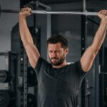 Man experiencing discomfort during an overhead press in a gym