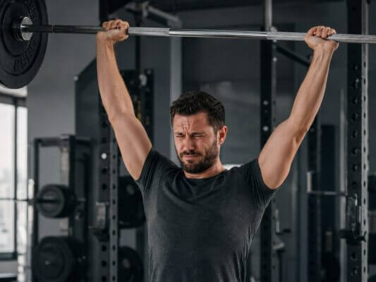 Man experiencing discomfort during an overhead press in a gym