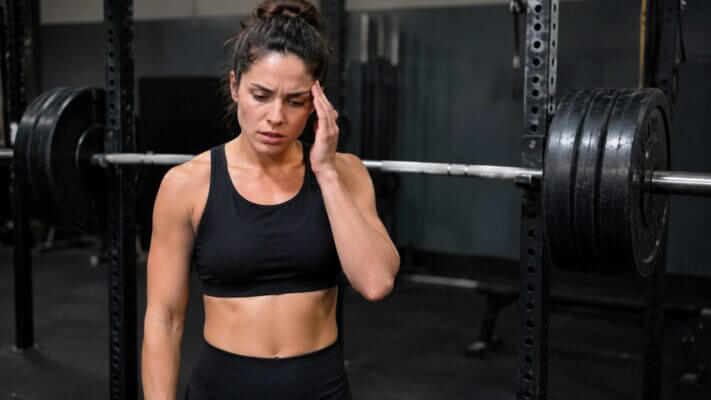 Athlete experiencing head pressure after a heavy squat set beside a barbell rack