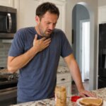 Western man experiencing reflux-like discomfort after eating peanut butter in a home kitchen