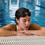 Swimmer resting at the edge of an indoor pool after a hard swim workout
