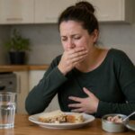 Western woman feeling nauseous at a kitchen table after eating a tuna sandwich, with an open tuna can and glass of water nearby in a natural realistic home setting.