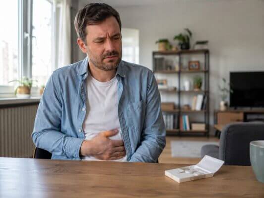 Western man holding his stomach beside an open pack of sugar-free gum at home, suggesting digestive discomfort after chewing xylitol gum.